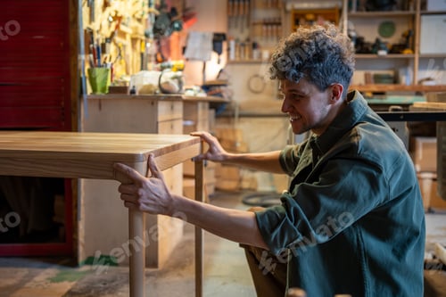 Preview: Carpentry workshop, male craftsman working. Professional artisan smiles, checking wooden table