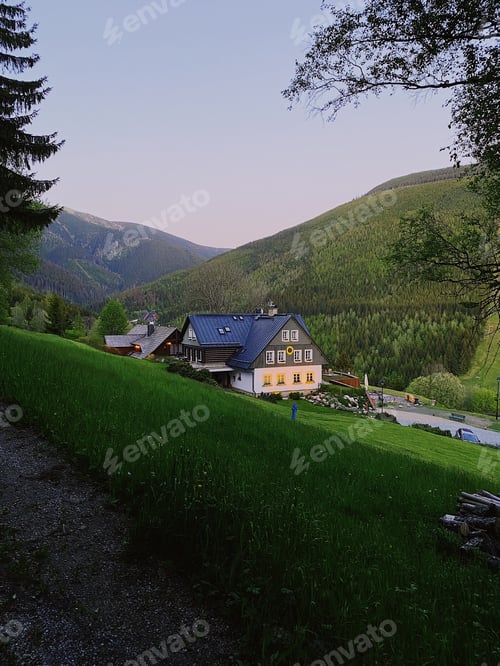 Preview: Countryside house in lush green mountains at dusk.