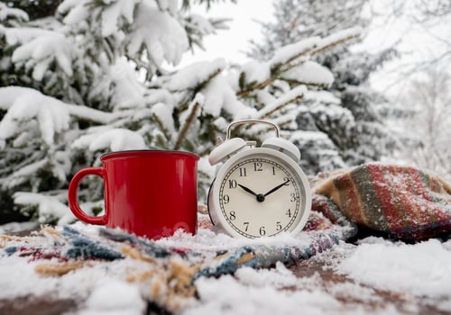 Preview: Red cup of coffee and vintage alarm clock with scarf on wooden table in blizzard