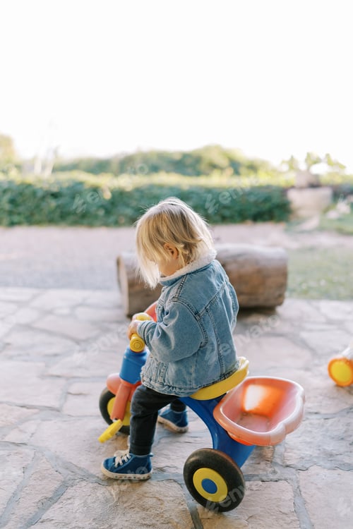 Preview: Little girl sits on a tricycle and looks at the steering wheel