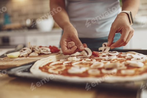 Preview: A woman's hands spread mushrooms on the pizza before baking