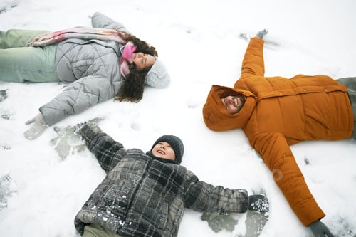 Preview: Family Lying on Snow Making Snow Angels and Smiling Outdoors