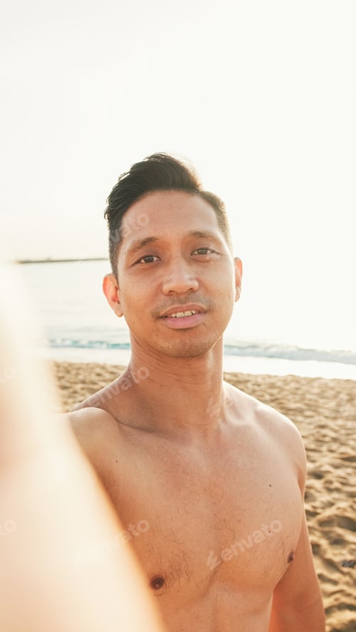 Preview: Close up of guy, an athlete with a naked torso standing on the beach makes a selfie on a smartphone