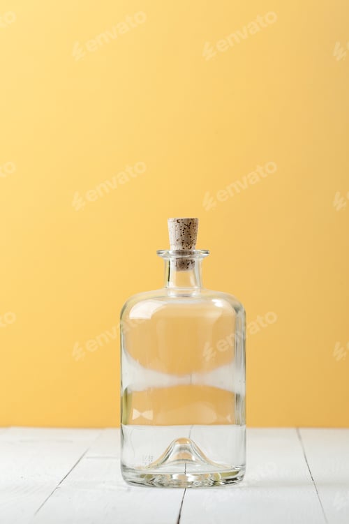 Preview: Empty glass bottle for rum on a light white-yellow background.