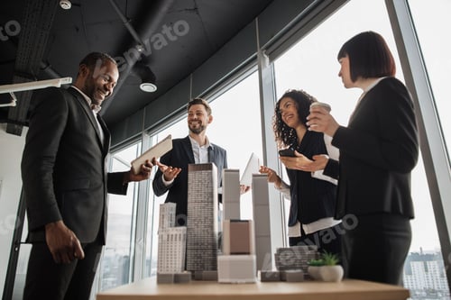 Preview: Multiethnic real estate agents, standing near table with city model in office with panoramic view