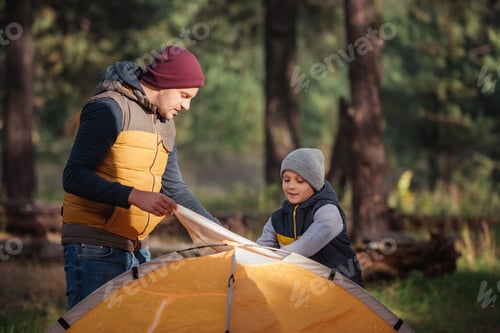 Preview: father and son putting up tent in autumn forest