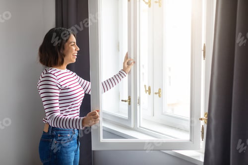 Preview: Portrait Of Young Smiling Arab Woman Opening Window At Home
