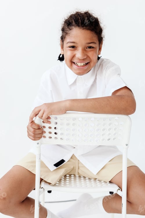 Visualização: Menino de camisa branca e shorts sentado na cadeira com as mãos nos joelhos em contemplação