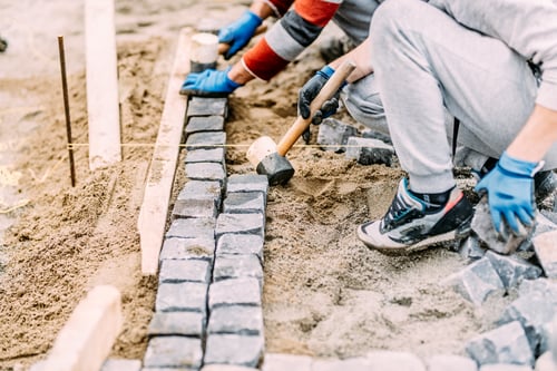 Preview: Industrial construction worker paving road with granite cobblestone using sand and rubber hammer