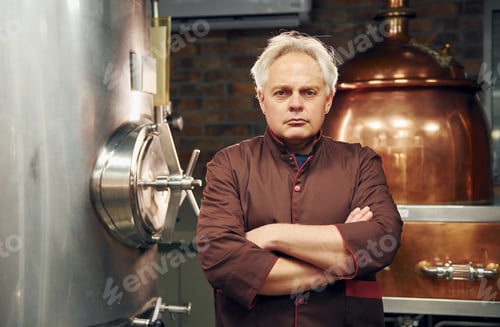 Preview: Retro style. Senior man is standing in the storage with equipment for beer