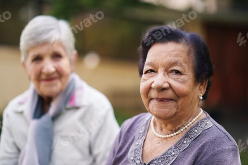 Preview: Two elderly women sitting on bench in park smiling happy life long friends enjoying retirement
