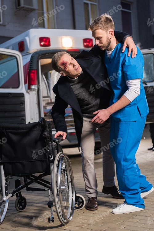 Preview: paramedic helping injured patient to sit in wheelchair
