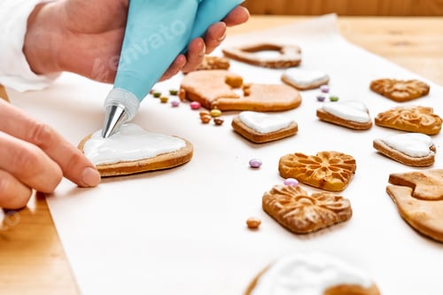 Preview: Woman decorating heart shaped cookies with frosting. Glazed festive homemade biscuits