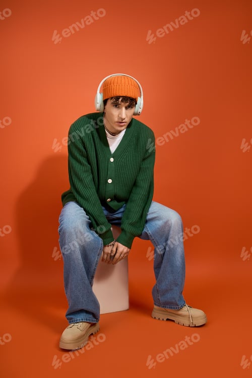 Preview: Handsome man showcases trendy outfit against vibrant orange backdrop with stylish accessories