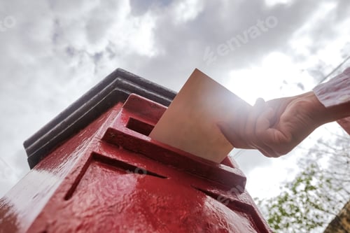 Preview: Closeup on a male hand putting a letter in a red letterbox.