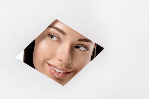 Preview: smiling young woman looking away through rhombus shaped hole on white