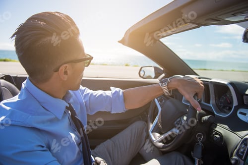 Preview: Young businessman driving convertible at coast