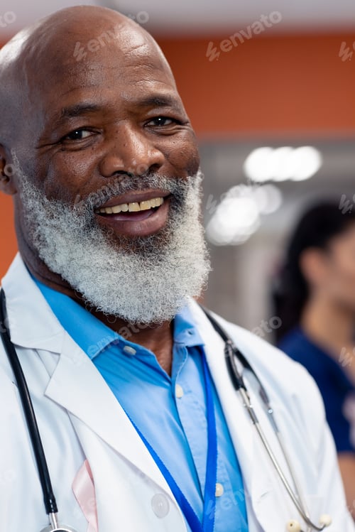 Preview: Vertical portrait of smiling senior male doctor with cancer ribbon in hospital ward, copy space