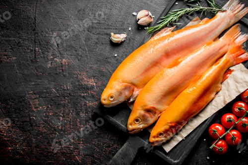 Preview: Raw trout on a cutting Board with tomatoes, rosemary and garlic cloves.