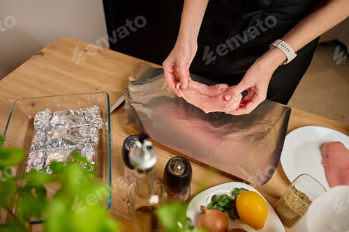 Preview: Woman placing raw chicken breast on foil in kitchen