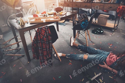 Preview: Cropped shot of drunk young woman lying on floor in messy room after party