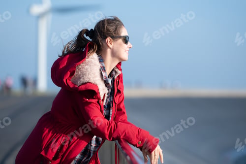 Preview: On the background of windmills, A young woman in a red jacket is enjoying her winter vacation.
