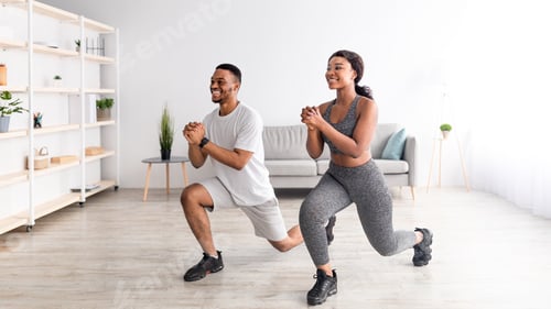 Preview: Domestic fitness. Full length of positive black couple doing lunges indoors, panorama