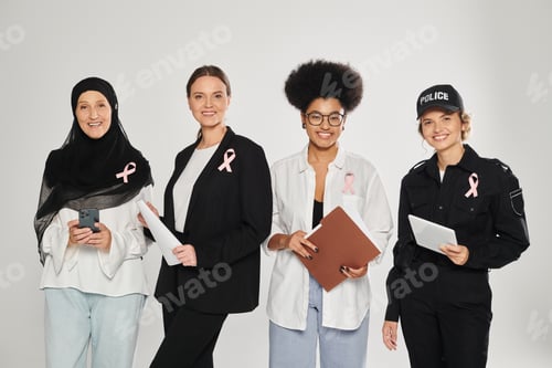 Preview: smiling different interracial women with pink ribbons holding devices and papers isolated on grey