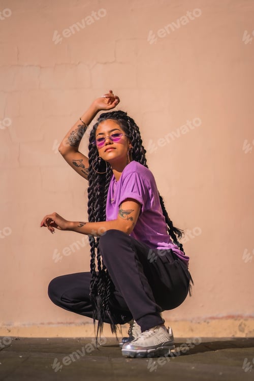 Preview: A dark-skinned young woman with long braids and purple glasses. In an urban shoot, on the ground