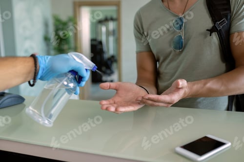 Preview: Unrecognizable athlete getting hand disinfection at gym's reception desk.