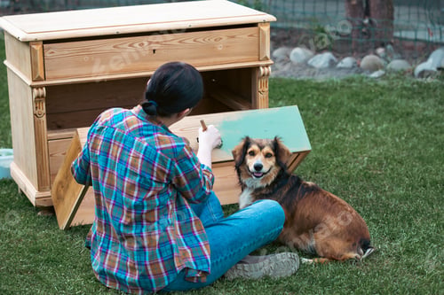 Preview: Woman painting a wooden furniture while sitting with her dog in the garden.
