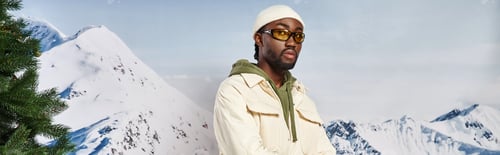 Preview: stylish good looking man in winter jacket and beanie with sunglasses looking at camera, banner