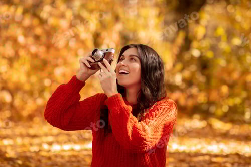Preview: Professional female photographer taking photos with retro camera outside on sunny autumn day