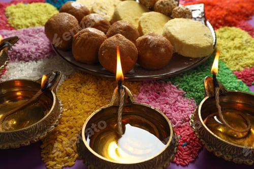 Preview: Diwali celebration. Tasty Indian sweets, diya lamps and colorful rangoli on table, closeup