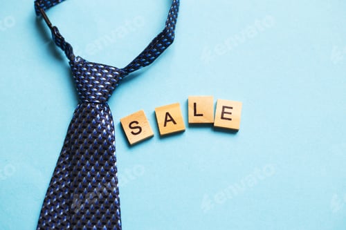 Preview: the word sale made by wooden cubes on a blue background with a tie.