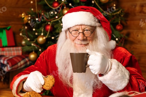 Preview: Happy Santa with mug of hot tea having drink and eating tasty homemade cookies
