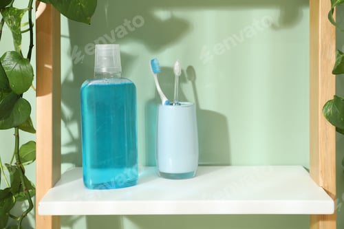 Preview: Bottle of mouthwash and toothbrushes on shelf in bathroom. Space for text