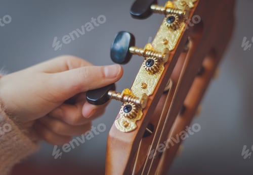 Preview: The girl twists the guitar peg while tuning the strings.