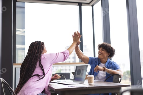 Preview: Diverse colleagues high-fiving at table with a laptop in a modern business office