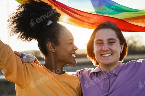 Preview: Happy women gay couple holding rainbow flag outdoor - Focus on right girl eyes