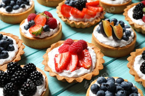 Preview: Many different berry tarts on blue wooden table. Delicious pastries