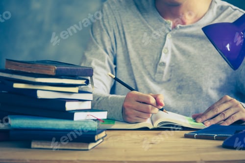 Preview: Close up of a man writing in notebook, Stack of old books on wooden desk. Vintage tone