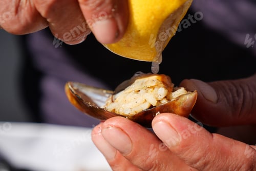 Preview: A hand squeezing fresh lemon juice onto a clam shell to enhance the culinary experience,