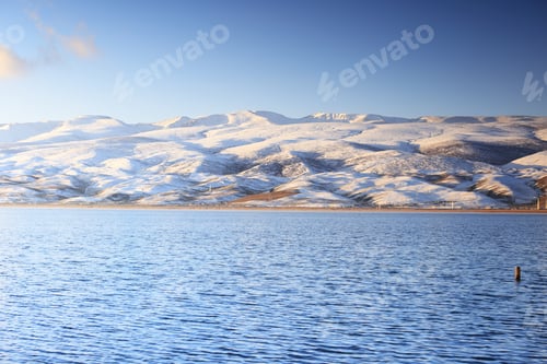 Preview: Scenic view of Qinghai Lake surrounded by snowy hills in China