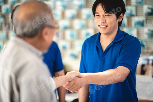 Preview: Young Asian male smiling car mechanic shaking hands with senior customer while standing
