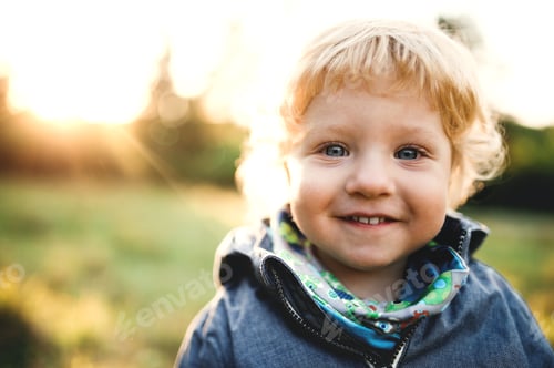 Preview: A little toddler boy standing outdoors on a meadow at sunset. Close-up.