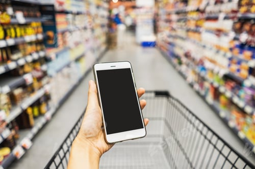 Preview: Hand holding smart phone with pushcart in supermarket