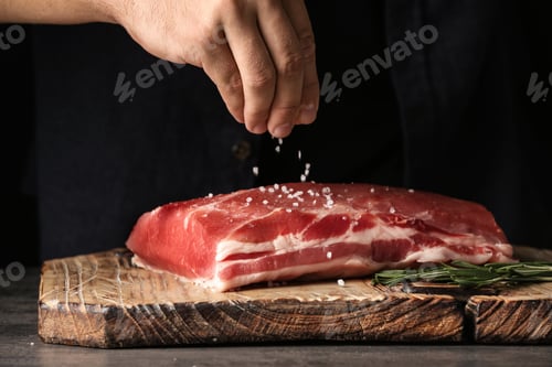 Preview: Man salting fresh raw meat on wooden board, closeup