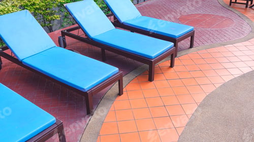 Preview: Row of blue sunbed lounger chairs on colorful stone tile floor decoration in poolside area at resort