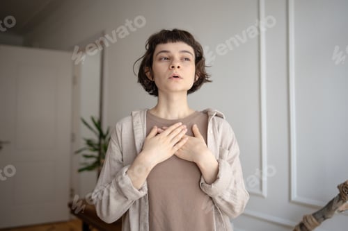 Preview: Young woman practicing stress relief, doing breathing exercises for calming, holding hands on chest.